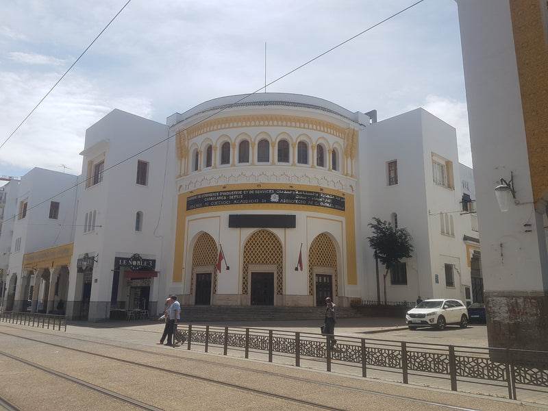 The white and yellow façade of the Chamber of Commerce on Boulevard Mohammed V in Casablanca, with pedestrians and tram tracks in the foreground.