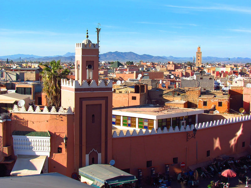 Ochre rooftops and minarets in Marrakech, with mountains on the horizon, Morocco.