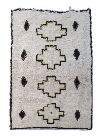 A rectangular woven rug with a cream-colored pile, featuring four large central stepped motifs and six small diamond motifs, outlined in olive green and finished with a black fringed border.
