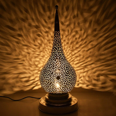 Decorative lamp with intricate design casting shadows on a textured wall.