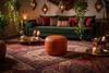 A cozy bohemian living room scene featuring a dark green velvet sofa with red and patterned pillows, a round brown leather pouf in the foreground, a large red and navy patterned oriental rug, and hanging lantern lights.