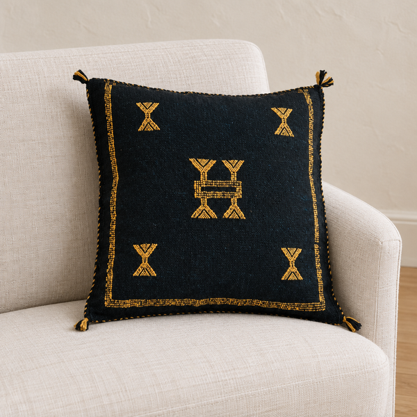 Sidi Omar Black pillow on an ivory linen armchair in soft natural daylight